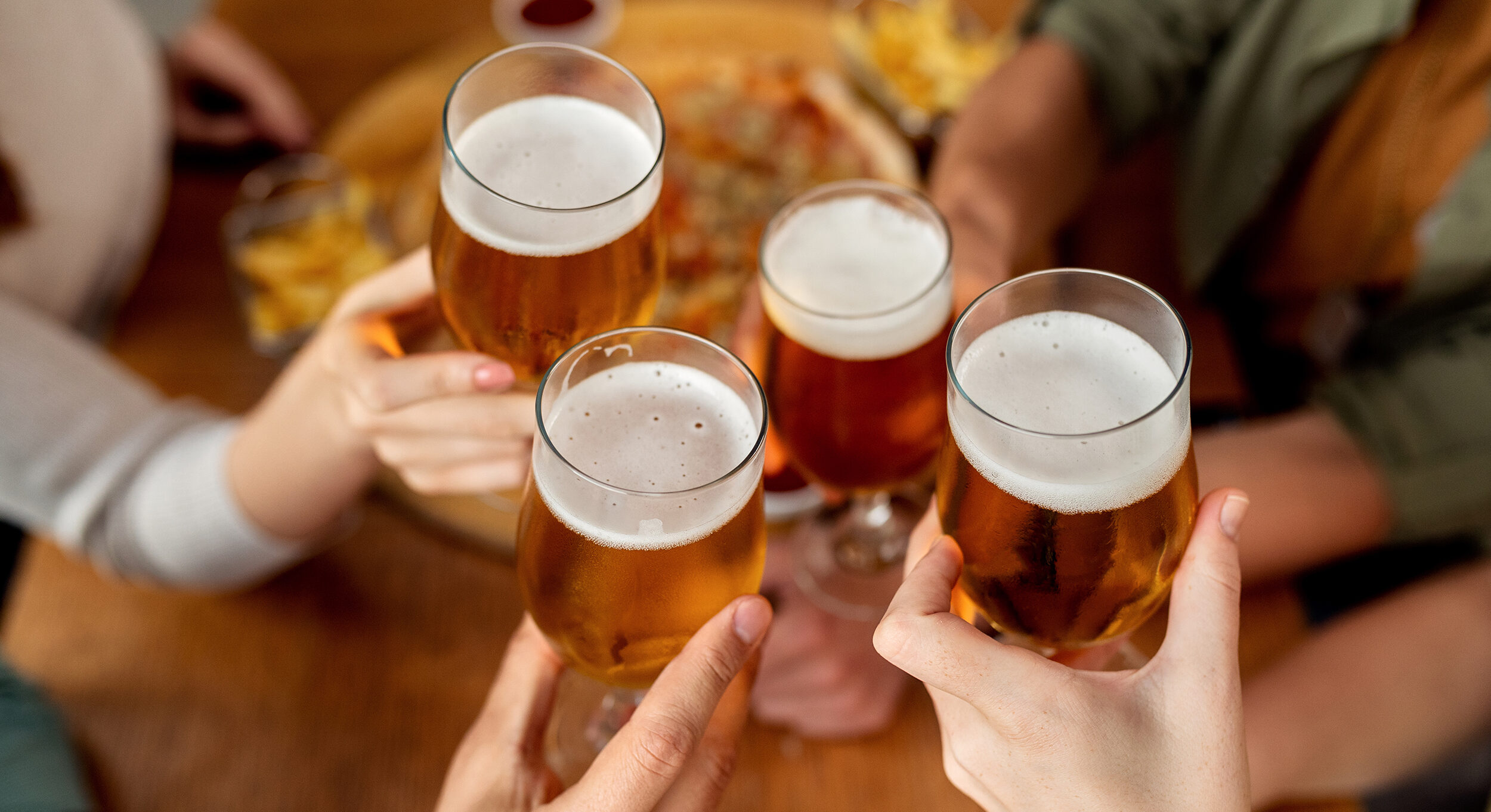 Close-up of friends celebrating and toasting with beer in a pub.